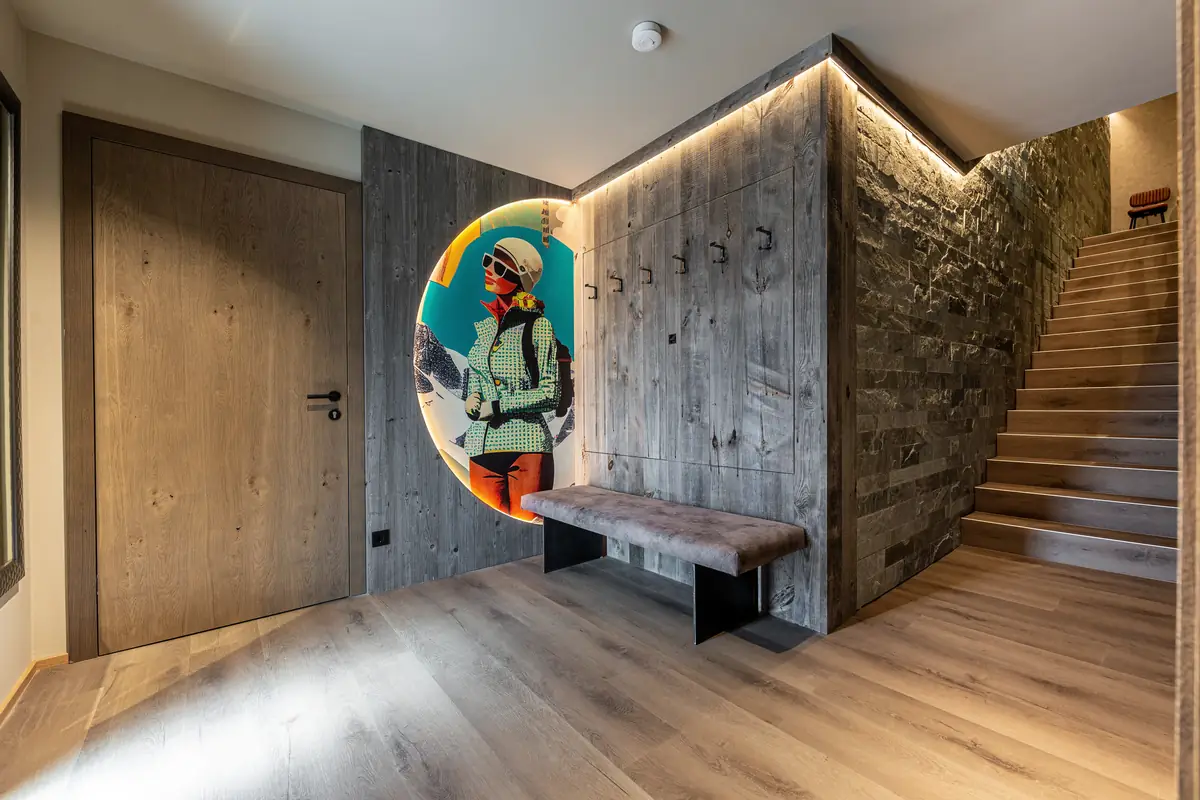 Eingang mit Altholz, Natursteinwand, Treppe und beleuchtetem Pop-Art-Bild einer Skifahrerin